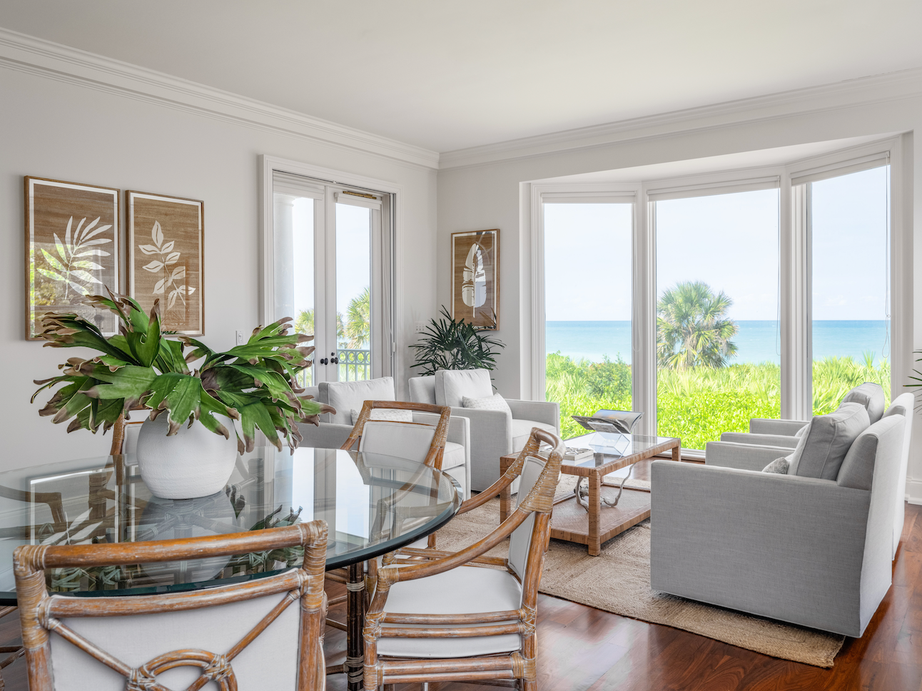Modern living room with glass dining table, chairs, and a view of the ocean.