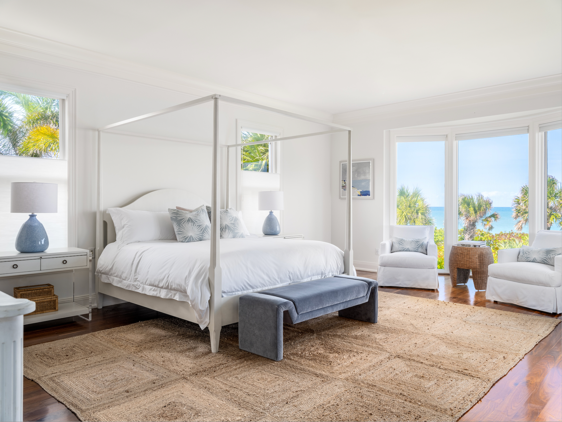 Modern bedroom with a four-poster bed, white bedding, and large windows with ocean view.